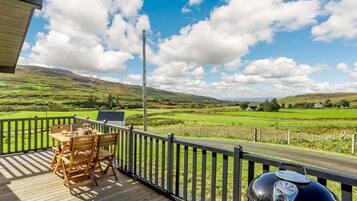 Une terrasse en bois avec une table et des chaises, donnant sur un paysage rural composé de champs et de maisons.