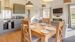 Une cuisine moderne avec un coin repas, des chaises en bois, une table dressée pour quatre personnes et un téléviseur fixé au mur.