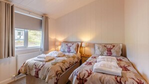 Une chambre avec deux lits, chacun recouvert d’une couvre-lit à motifs de cerfs, une fenêtre avec des rideaux et un luminaire au plafond.