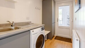 Une cuisine compacte équipée d’un évier, d’un lave-linge et d’une porte donnant sur un balcon.