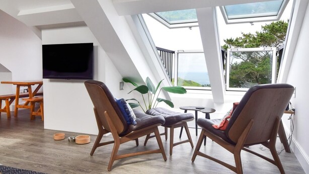 A modern living room with a high ceiling, skylights, a flat-screen TV, wooden furniture, and a view of the outdoors. - 3 Bed in Woolacombe (oc-87573) (Mortehoe)