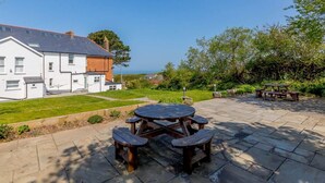 A house with a patio area featuring a wooden table and benches. - 3 Bed in Woolacombe (oc-87573) (Mortehoe)