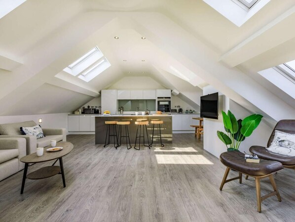 En moderne loftlejlighed med et køkken, spiseområde og opholdsstue, med ovenlysvinduer og en stor plante.