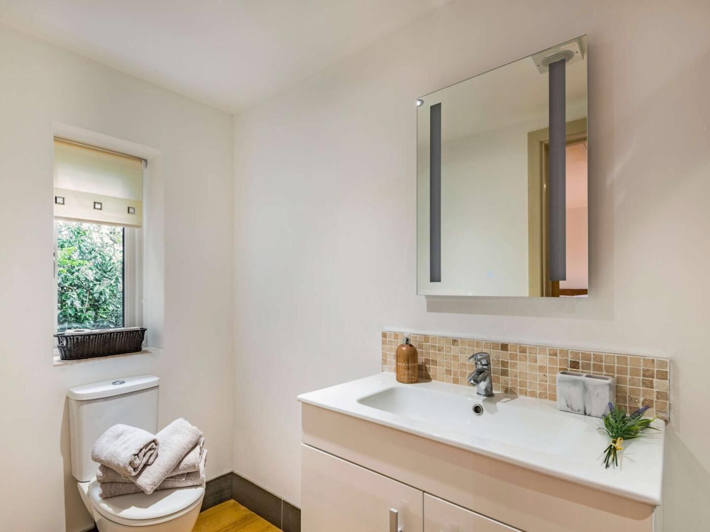 Une salle de bain avec des toilettes, un lavabo, un miroir et une fenêtre.