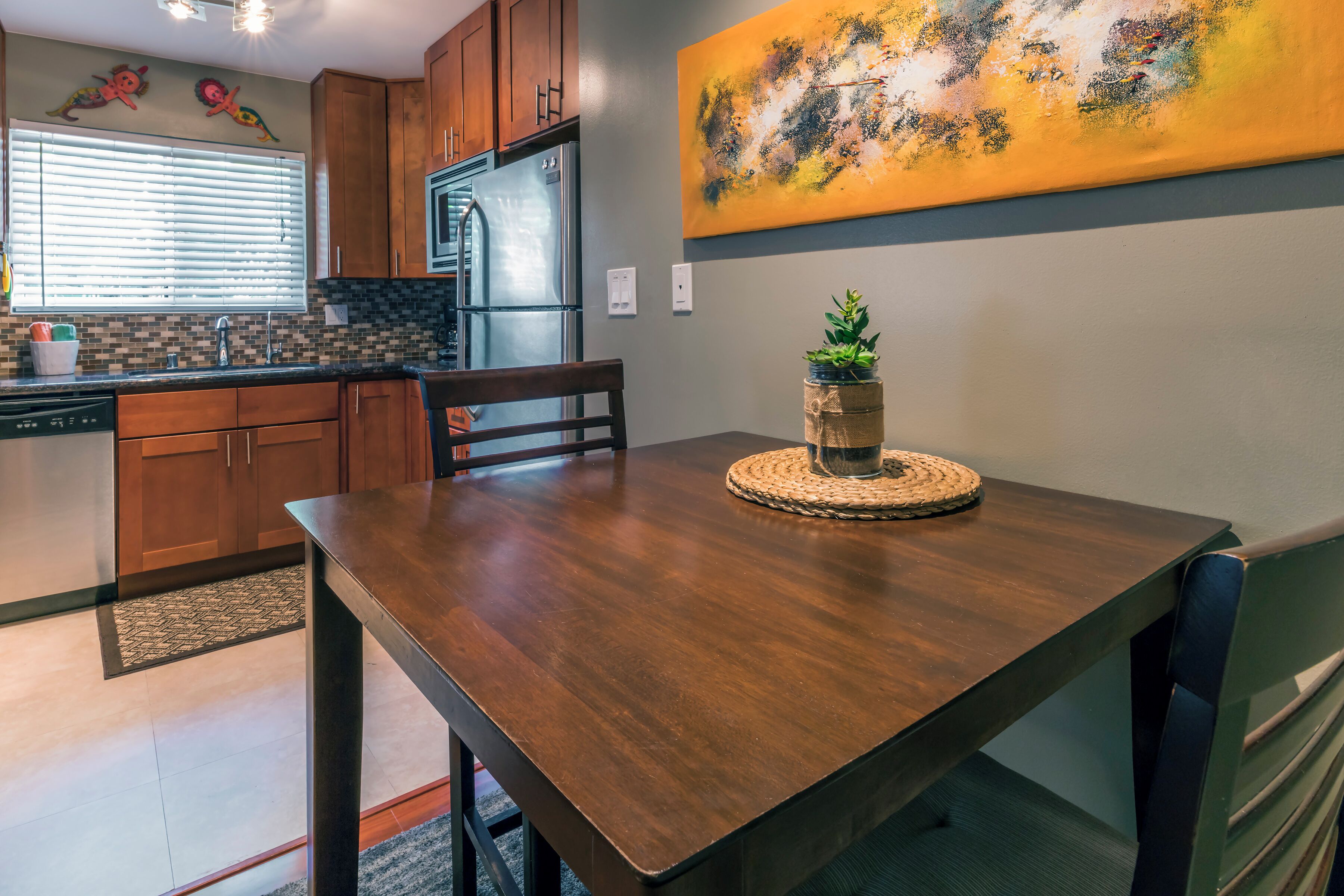 A modern kitchen with wooden cabinets, a stainless steel refrigerator, and a dining table with chairs.