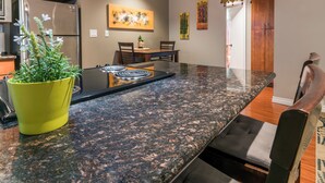 A kitchen with a granite countertop, a stainless steel refrigerator, and wooden cabinets. - Quiet PB Retreat w/ Cal KING Bed, AC & Parking (San Diego)