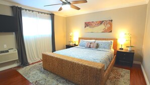 A bedroom with a bed, a ceiling fan, a nightstand with a lamp, and a wall-mounted air conditioner. - Quiet PB Retreat w/ Cal KING Bed, AC & Parking (San Diego)