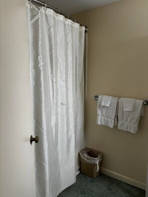 A bathroom with a shower curtain, a towel rack with towels, and a trash bin.