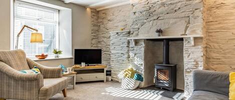 A cozy living room with a stone wall, a fireplace, a television, and a comfortable seating area.