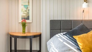 A bedroom with a bed, a bedside table with a vase of flowers, a wall-mounted lamp, and a framed picture. - 1 Bed in Wadebridge (oc-87740) (Wadebridge)