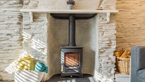 A stone fireplace with a modern wood-burning stove, a white mantel shelf, and a basket of firewood. - 1 Bed in Wadebridge (oc-87740) (Wadebridge)
