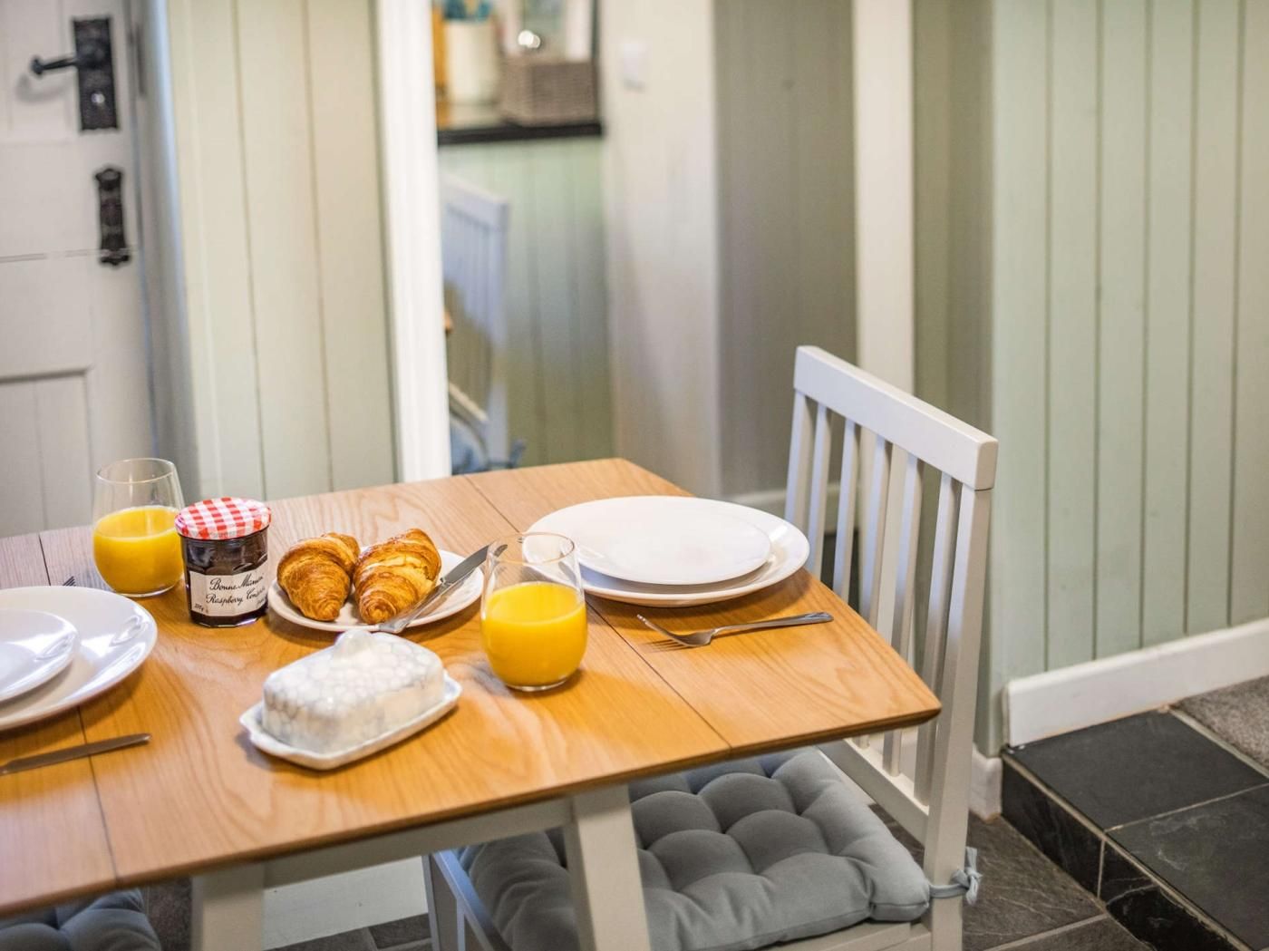 A breakfast table with croissants, a glass of orange juice, and a jar of jam.