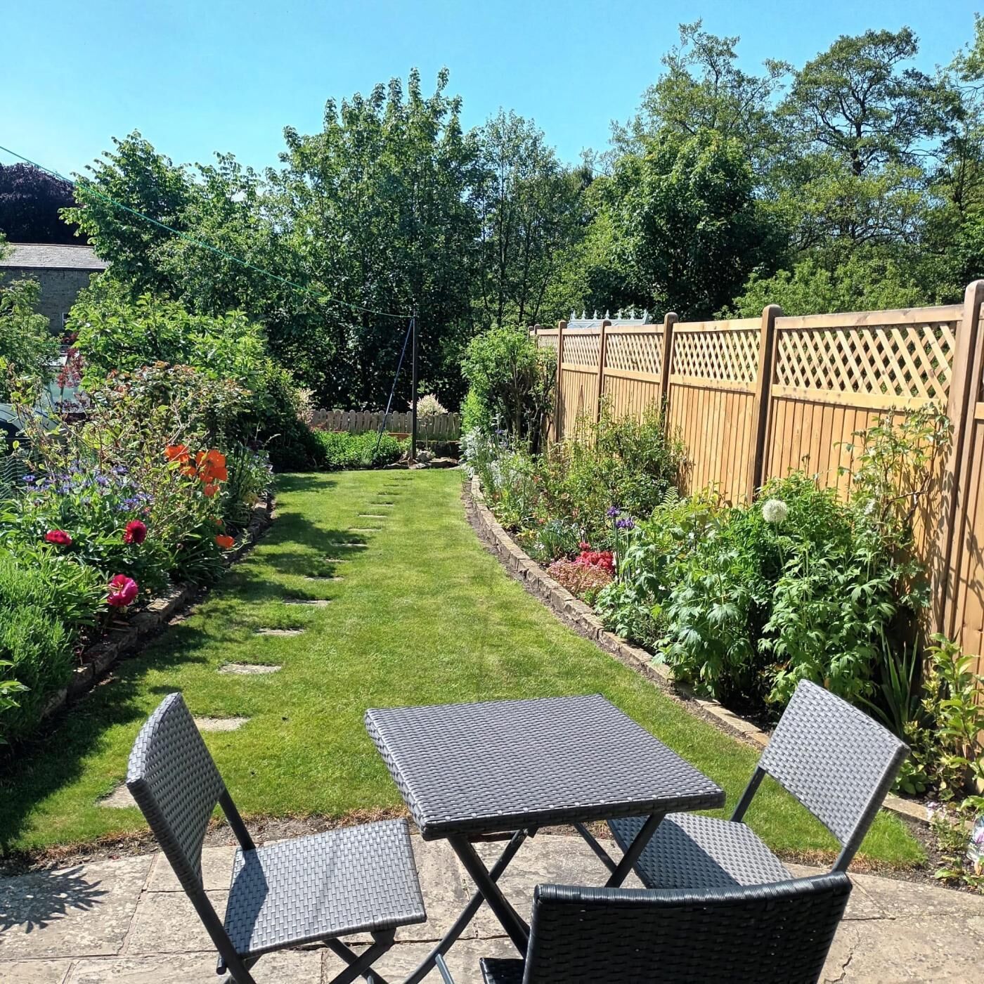 Un jardin avec une pelouse, une clôture en bois et une table avec des chaises.