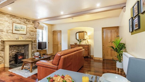 A cozy living room with a fireplace, a television, a sofa, and a dining area with croissants and juice. - 1 Bed in Crieff (oc-87497) (Crieff)