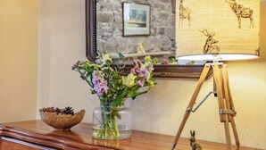 A wooden dresser with a vase of flowers, a lamp with deer designs, and a mirror reflecting a stone wall and picture frame. - 1 Bed in Crieff (oc-87497) (Crieff)