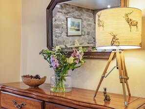 A wooden dresser with a vase of flowers, a lamp with deer designs, and a mirror reflecting a stone wall and picture frame. - 1 Bed in Crieff (oc-87497) (Crieff)