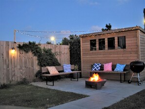 Une terrasse en bois avec un foyer, des sièges d’extérieur et des guirlandes lumineuses.