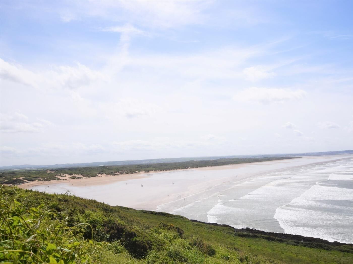 A coastal landscape with a beach, grassy areas, and a clear sky.