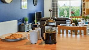 Eine Kaffeemaschine auf einem Tisch mit einem Teller Kekse und zwei weißen Tassen.