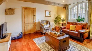 Ein Wohnzimmer mit Holzboden, einer Couch, einem Couchtisch, einem Fernseher und einer Tür.