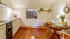 Eine Küche mit Herd, Backofen und Spüle; ein Esstisch mit Frühstücksgebäck; ein Fenster mit Aussicht; und ein Regal mit Gläsern.