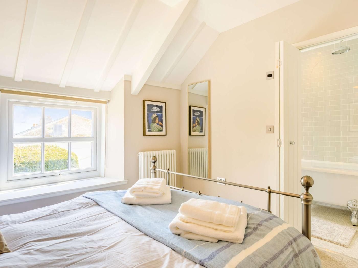 A bedroom with a bed, a window, a radiator, and a door leading to a bathroom.