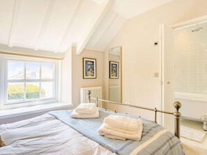 Ein Schlafzimmer mit Bett, Fenster, Heizkörper und einer Tür zu einem Badezimmer.