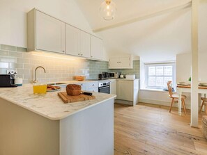 A modern kitchen with white cabinets, a marble countertop, and a wooden dining table. - 1 Bed in Bridport (oc-87527) (Charmouth)