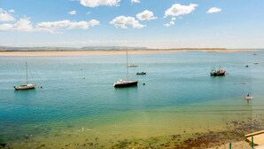 Una masa de agua tranquila con varias embarcaciones ancladas, una playa arenosa al fondo y un cielo despejado.