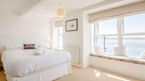 Una habitación de hotel con una cama grande, un asiento junto a la ventana, un radiador y una lámpara colgante.