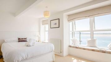 A hotel room with a large bed, a window seat, a radiator, and a hanging light fixture.