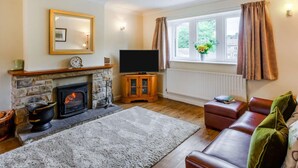 Ein Wohnzimmer mit Kamin aus Stein, einem Fernseher, einer Couch und einem Fenster mit Vorhängen.
