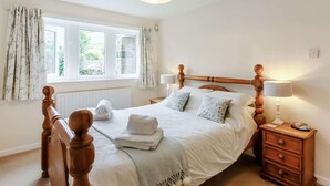 Ein Schlafzimmer mit hölzernem Bettgestell, einem Nachttisch mit Lampe, einem Fenster mit Vorhängen und einer Heizung.
