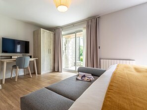 Een moderne hotelkamer met een flatscreen televisie, een bureau, een grijze bank en een groot raam met gordijnen.