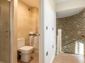 Een badkamer met een toilet, een douche en een stenen muur.