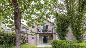 A stone house with a balcony, a grassy yard, and a tree.