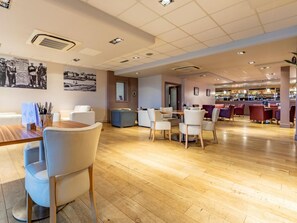Een ruim restaurant met houten vloeren, witte en rode zitplaatsen en een bar.