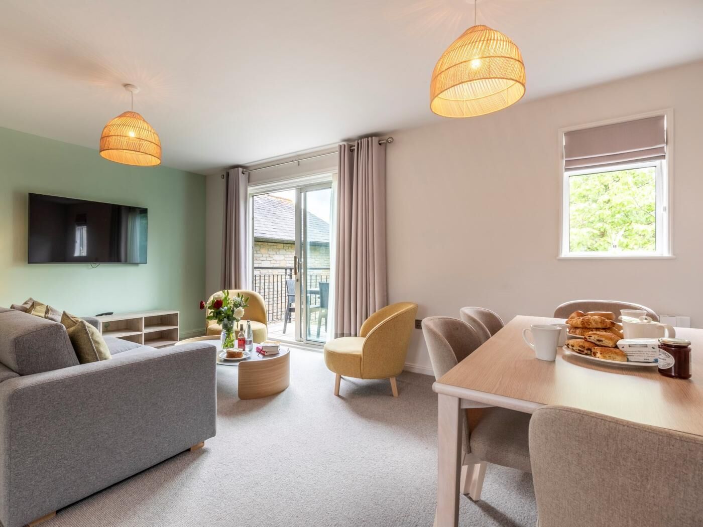 Ein modernes Wohnzimmer mit Sofa, einem Esstisch mit Stühlen, einem an der Wand montierten Fernseher und einem Balkon mit Blick.