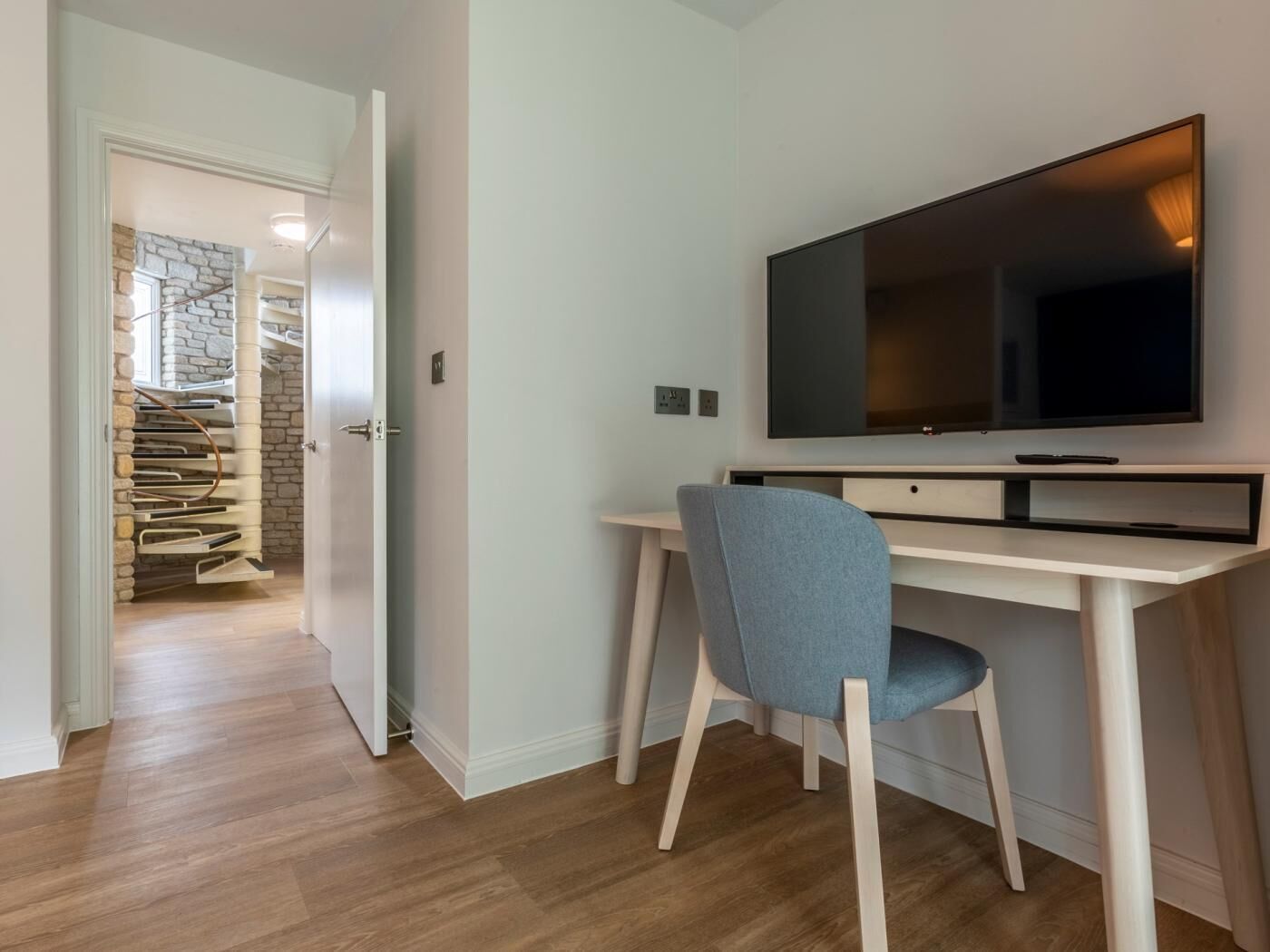 A modern room with a wooden desk, a large flat-screen TV, and a spiral staircase in the background.