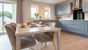 A modern kitchen with grey cabinets, a stainless steel range hood, and a dining area with a table set for breakfast. - 2 Bed in Saltash (oc-87704) (Saint Mellion)