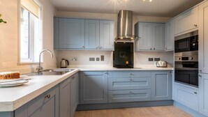 A modern kitchen with grey cabinets, a stainless steel range hood, and built-in appliances. - 2 Bed in Saltash (oc-87704) (Saint Mellion)