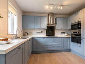 A modern kitchen with grey cabinets, a stainless steel range hood, and built-in appliances. - 2 Bed in Saltash (oc-87704) (Saint Mellion)