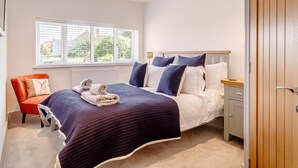 Un dormitorio con cama, mesitas de noche, una silla, una ventana y una puerta.