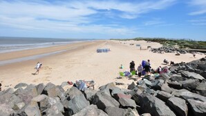 Una playa con un primer plano rocoso, una extensión de arena y un cielo despejado.