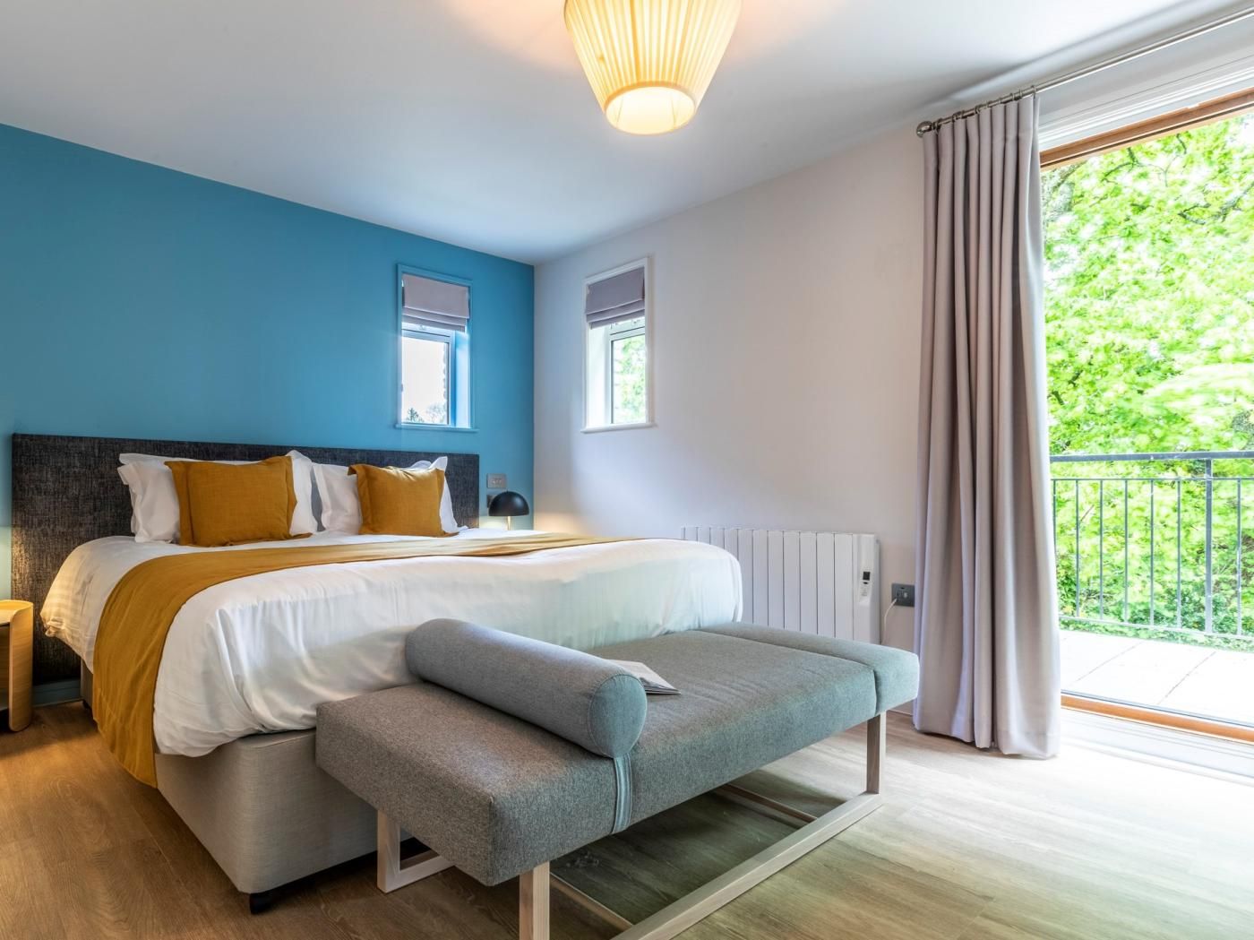 Camera da letto moderna con un letto grande, una panca, due finestre e vista sul verde circostante.