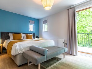 Un dormitorio moderno con una cama grande, un banco, dos ventanas y vistas a la vegetación.