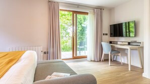 Quarto de hotel moderno com cama, escrivaninha, poltrona e televisão.