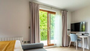A modern room with a sofa, a desk, a chair, a television, and a sliding glass door to a balcony. - 2 Bed in Saltash (oc-87706) (Saint Mellion)