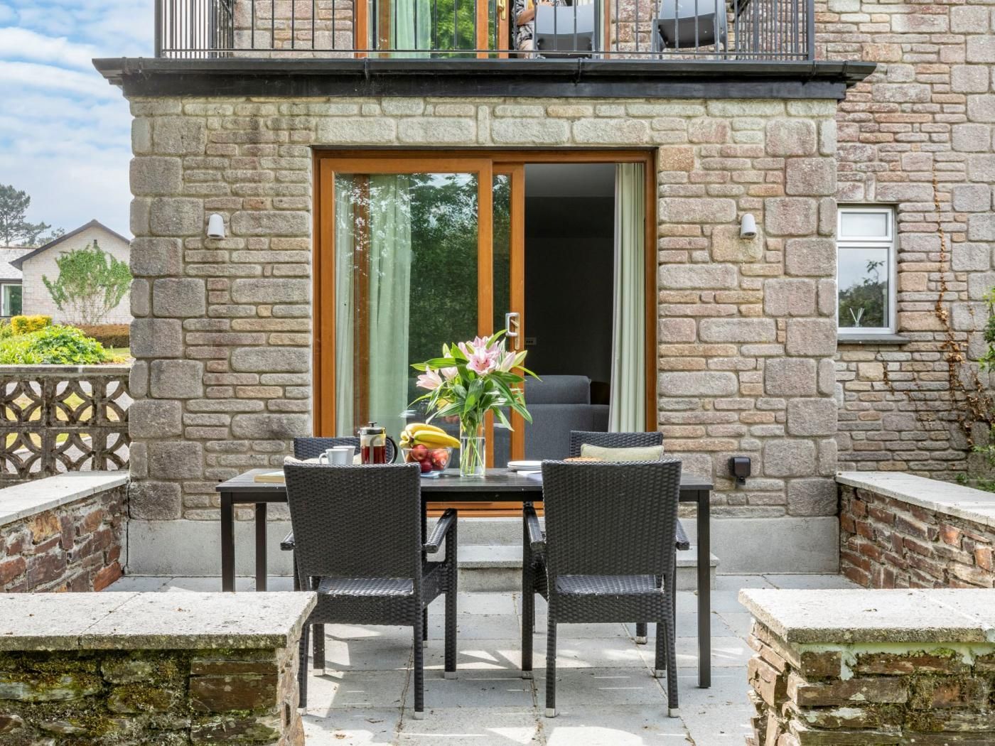 Een terras buiten, met een stenen muur, een tafel met stoelen en uitzicht op het huis.