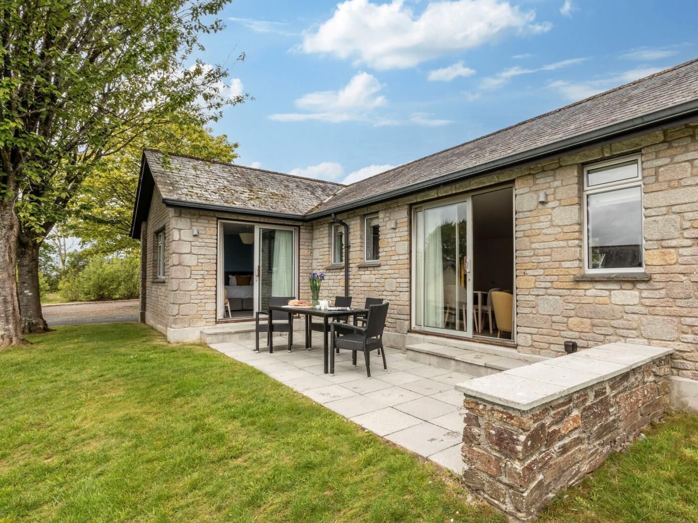 A stone building with a patio, a table with chairs, and a grassy area.